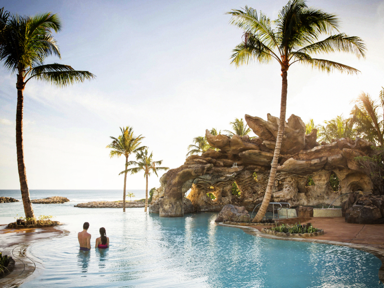 Couple in resort pool in Hawaii looking at palm trees and ocean